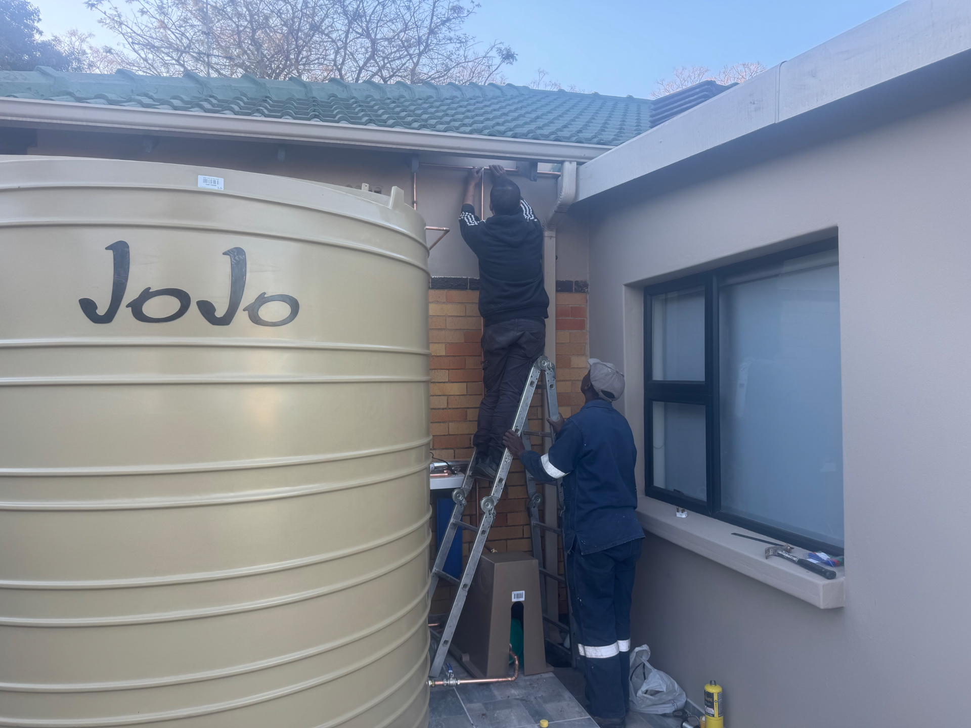 Plumbers X team installing a JoJo water tank and pipework at a home